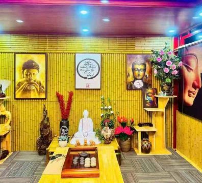 A calming zen-inspired interior featuring a synthetic bamboo wall with natural wood texture and warm tone, accented by soft purple-blue gradient lighting. The space includes a serene Guanyin statue, traditional tea set, Buddhist artwork, and wooden décor, creating a harmonious blend of Eastern spirituality and modern design.