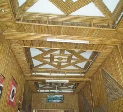 An immersive corridor entirely crafted from warm-toned synthetic bamboo. Its layered grille ceiling, centered with a geometric star-shaped light panel, establishes a captivating rhythm. The elongated bamboo framework and dancing light create a serene, textured passage that feels like walking through a secret bamboo forest.