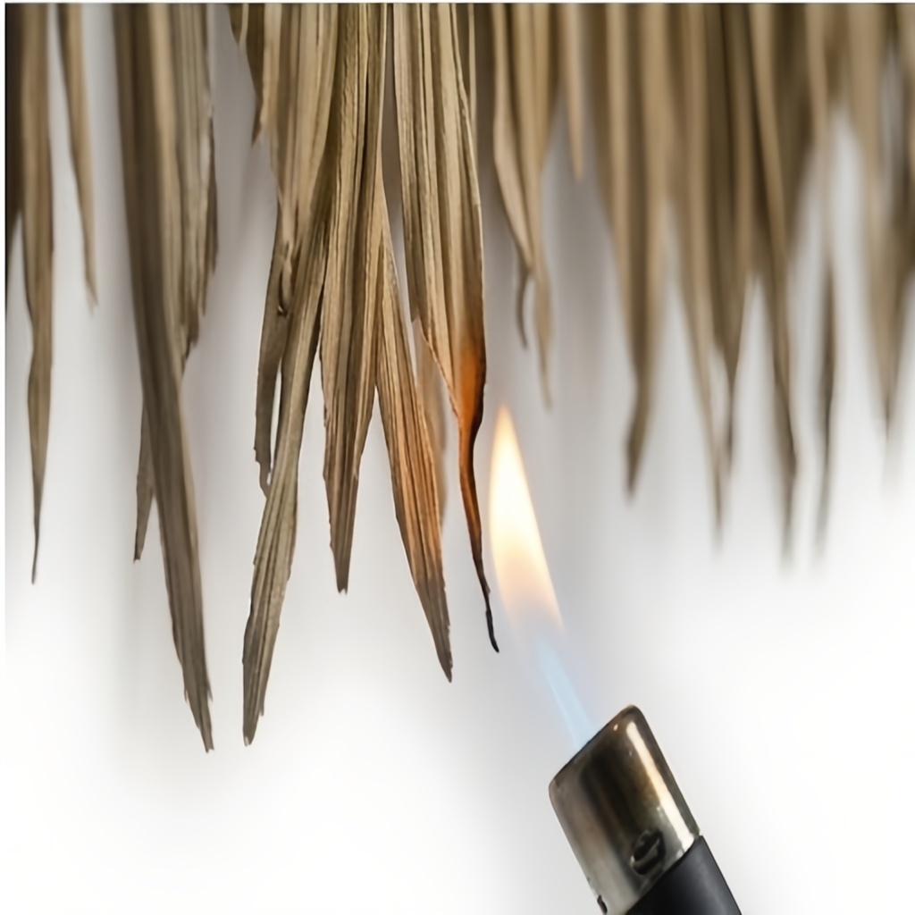 A close-up view showing the fringe tips of the synthetic palm thatch panel from image_1.png resisting ignition when a small, controlled micro-torch flame is brought near, demonstrating its fire-retardant safety feature.