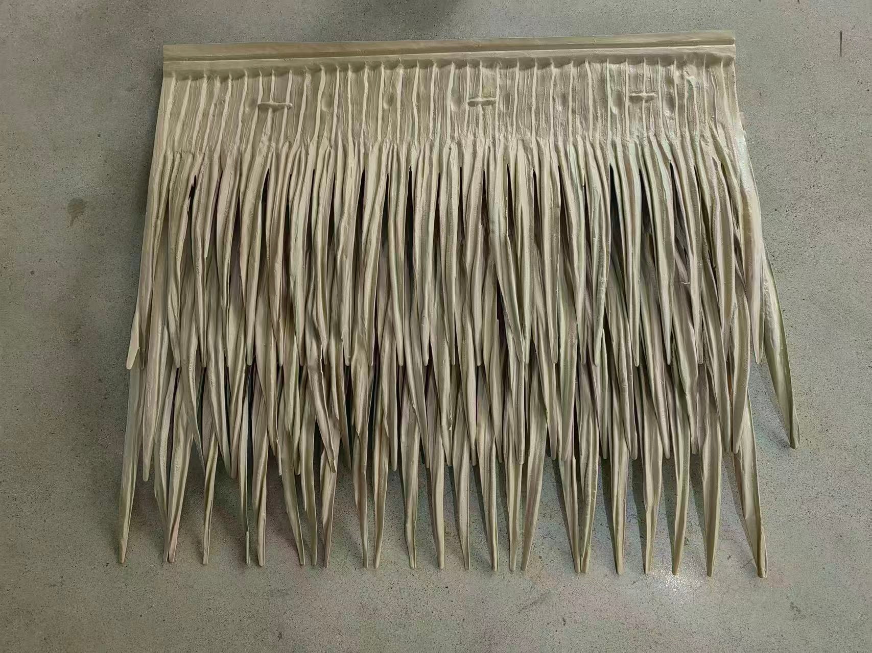 An overhead, detailed photograph of a single, beige-colored synthetic Mexican palm leaf thatch roofing panel. The panel features multiple overlapping rows of pointed, textured leaf sections designed to realistically mimic natural thatch. It is attached to a solid, molded header at the top with pre-drilled holes, all resting flat on a neutral grey concrete background. This panel is intended to create a tropical palapa-style roof using artificial materials.