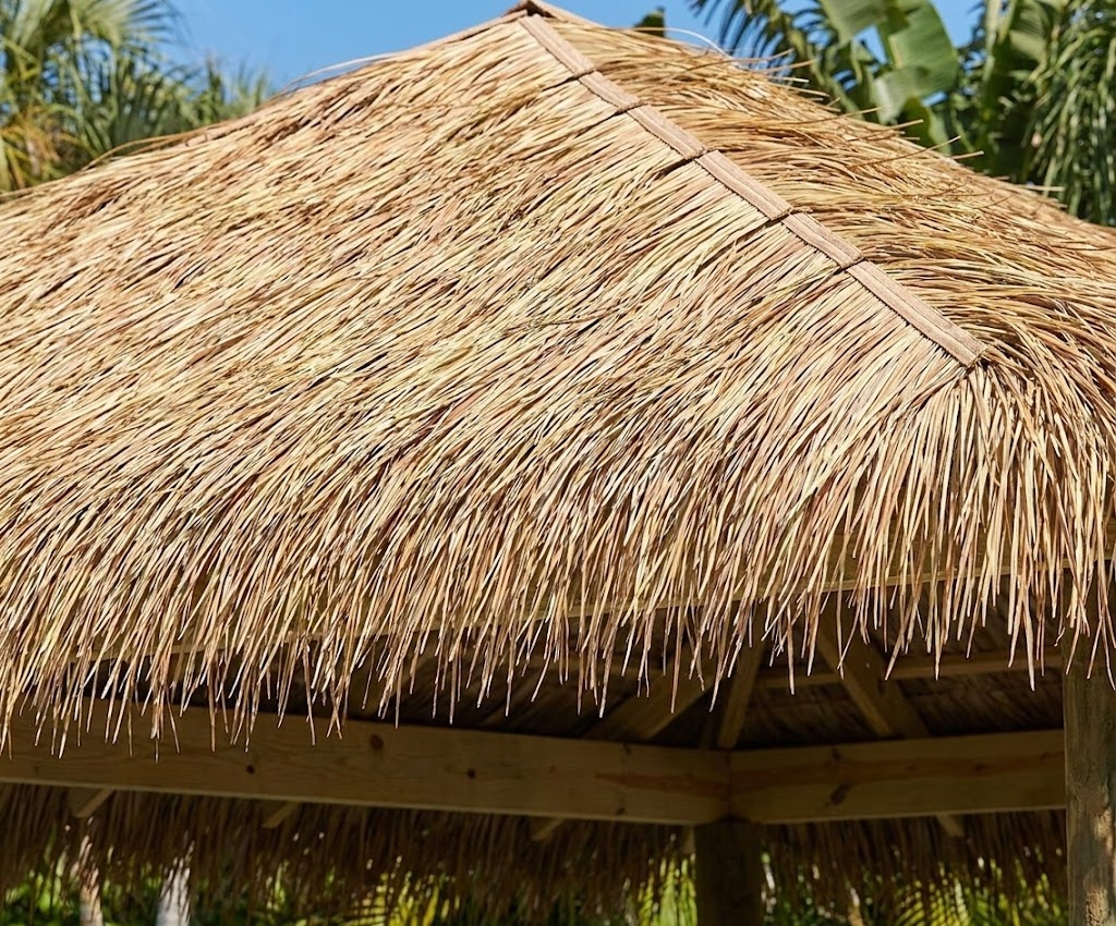 Close-up view of a tropical tiki hut roof newly renovated and completely covered with synthetic thatch replacement panels, featuring the tan and straw-yellow artificial grass texture from image_18.png, laid flat in overlapping rows under sunlight.